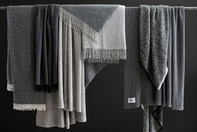 Eine Auswahl hochwertiger Decken und Plaids in Grau- und Schwarztönen mit verschiedenen Texturen.
