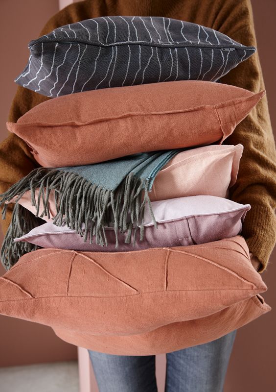 Stapel farbiger Kissen und eine Decke in warmen Erdtönen.