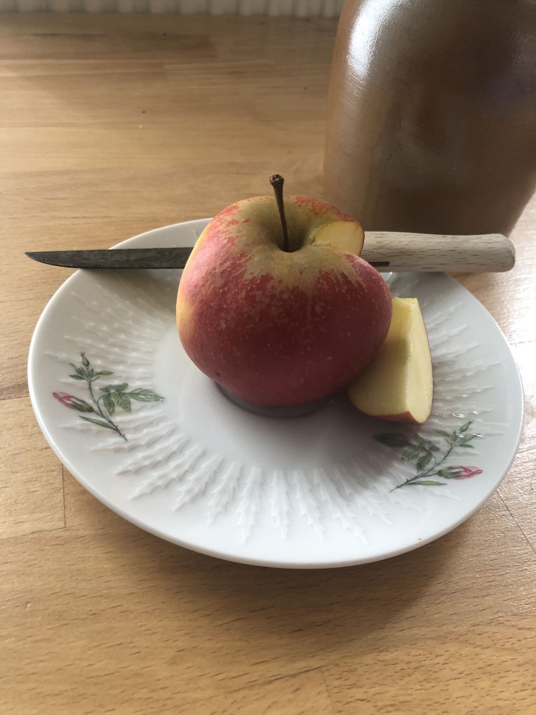 Roter Apfel, angeschnitten, auf weißem Teller mit Messer auf Holztisch.