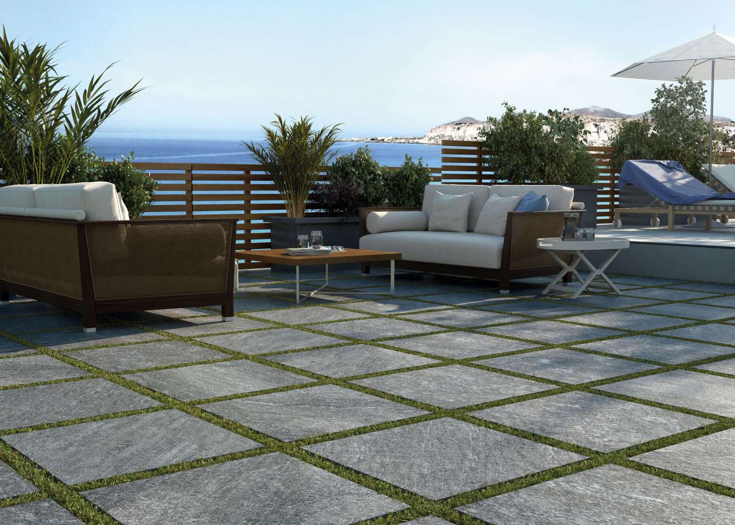 Graue Outdoor-Fliesen mit Grasfugen auf einer Terrasse am Meer.
